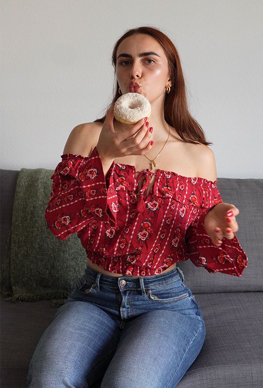 La coach sentada en un sofá sosteniendo un donut azucarado